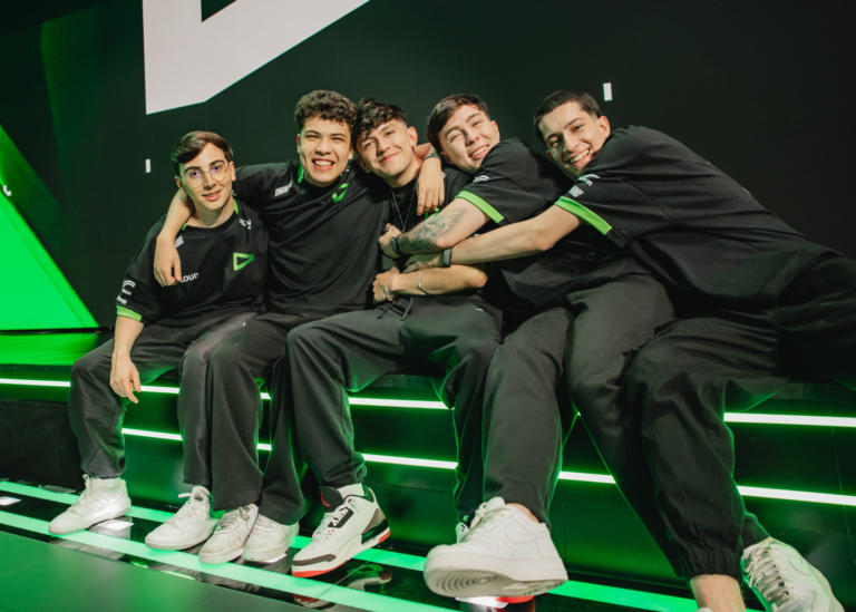Fotografia dos jogadores da equipe LOUD de Valorant comemorando no palco do VCT Americas. Eles estão abraçados vestindo o uniforme verde e preto da organização, com os telões do campeonato ao fundo, ilustrando a vitória nos playoffs